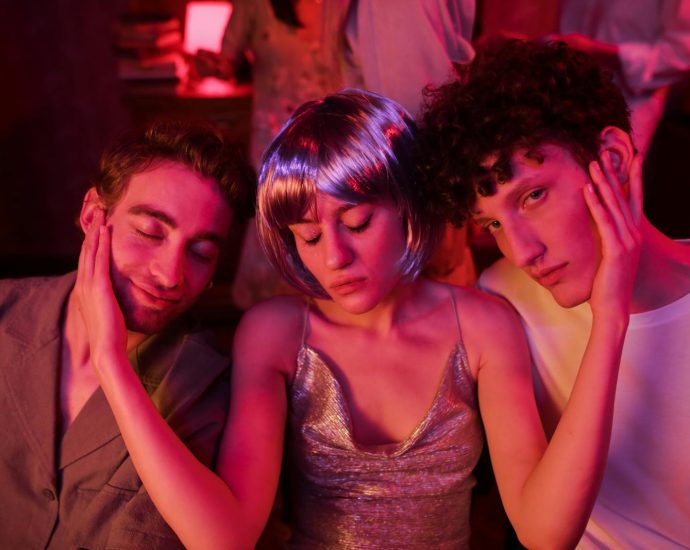 Three friends in neon lighting enjoying a vibrant night out, embracing together in a relaxed atmosphere.