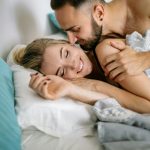Happy couple embracing in bed, showcasing love and affection in a cozy home setting.