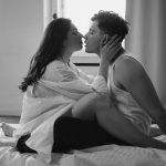 Monochrome image of a romantic couple kissing on a bed in an intimate setting. Captures love and passion.