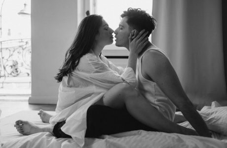 Monochrome image of a romantic couple kissing on a bed in an intimate setting. Captures love and passion.