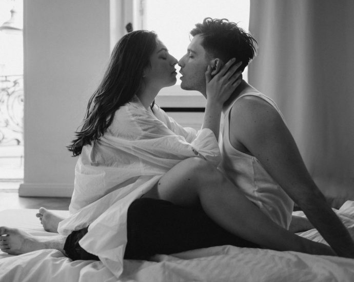 Monochrome image of a romantic couple kissing on a bed in an intimate setting. Captures love and passion.