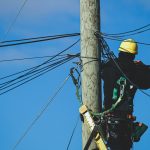 man in black jacket and yellow helmet on brown wooden post under blue sky during daytime