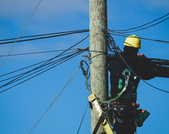 man in black jacket and yellow helmet on brown wooden post under blue sky during daytime