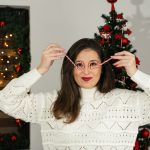 a woman holding a pair of glasses in front of a christmas tree