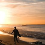 silhouette of man carrying surfboard running on shore