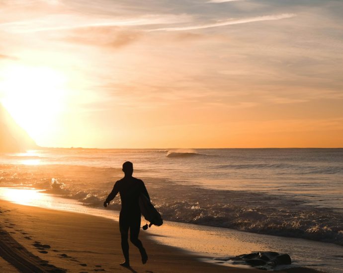 silhouette of man carrying surfboard running on shore