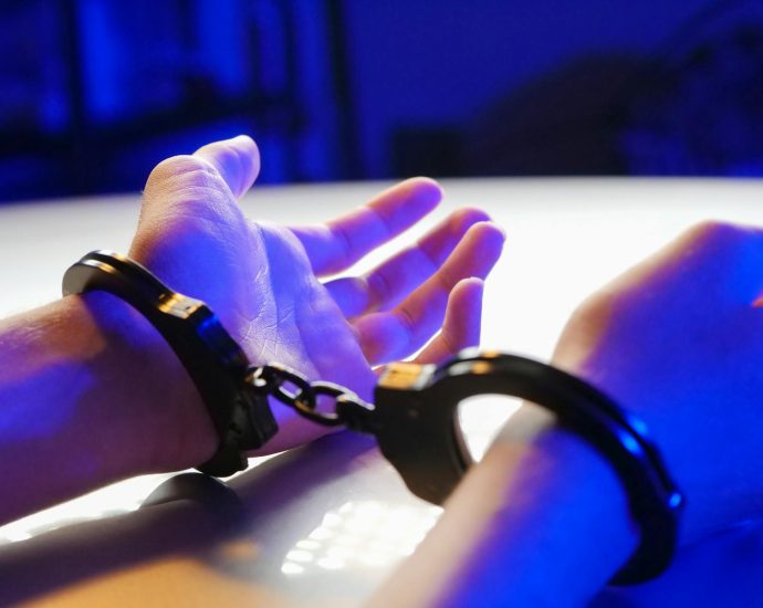 A close-up image of handcuffed hands under blue lighting, symbolizing law enforcement.