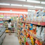 A woman browsing snack shelves at a supermarket, surrounded by various chips packages.