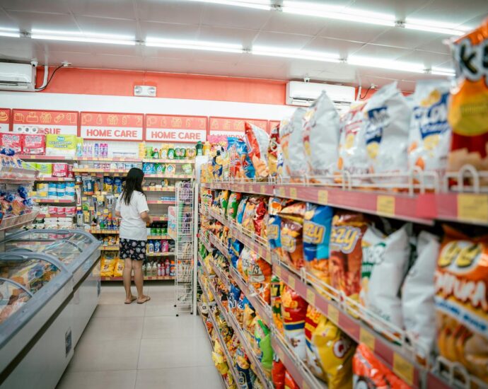 A woman browsing snack shelves at a supermarket, surrounded by various chips packages.