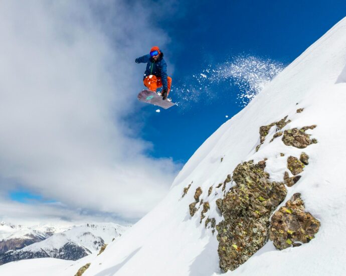 man in red jacket and blue pants sitting on snow covered mountain during daytime