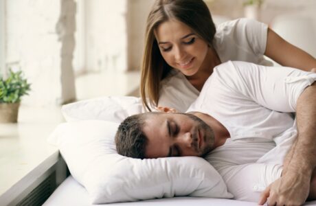 A woman watches a man sleeping in bed.