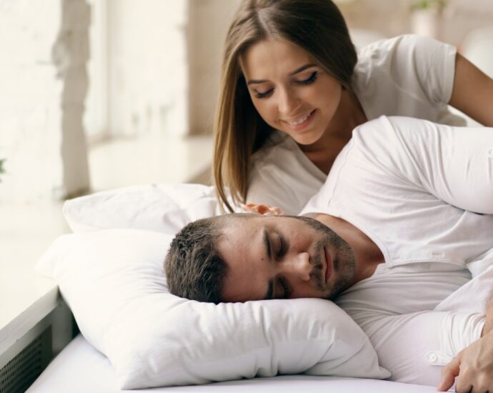 A woman watches a man sleeping in bed.