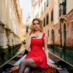 Young woman in red dress riding gondola in venice canal.