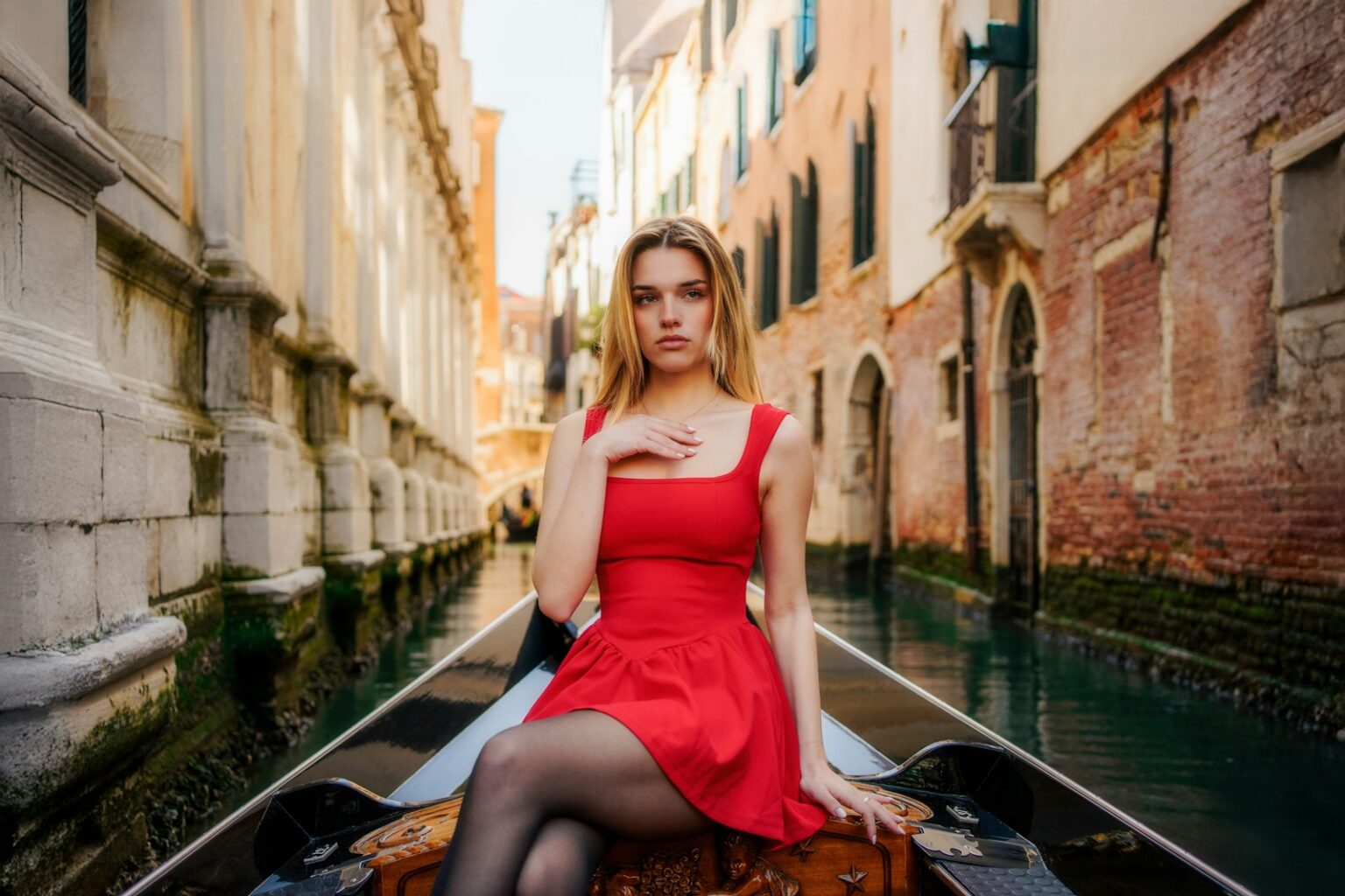Young woman in red dress riding gondola in venice canal.
