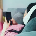 woman in pink shirt lying on bed holding smartphone