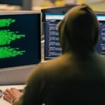 Hacker in hoodie working on multiple computer screens