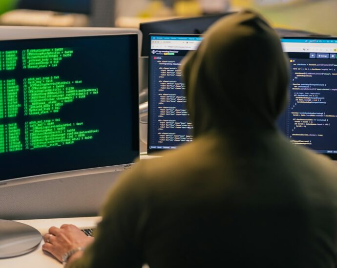Hacker in hoodie working on multiple computer screens
