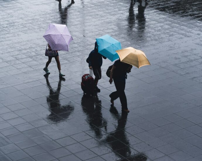 selective color photography of three person holding umbrellas under the rain