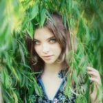 Young woman peeking through green leaves