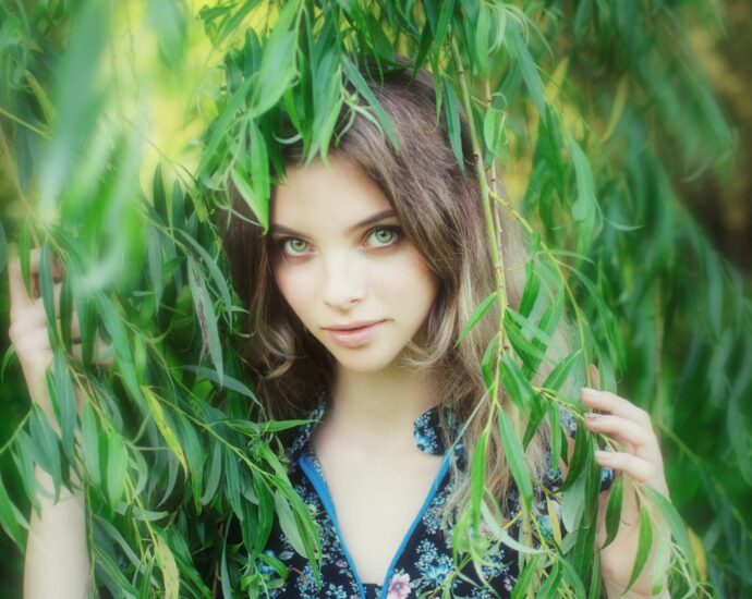 Young woman peeking through green leaves