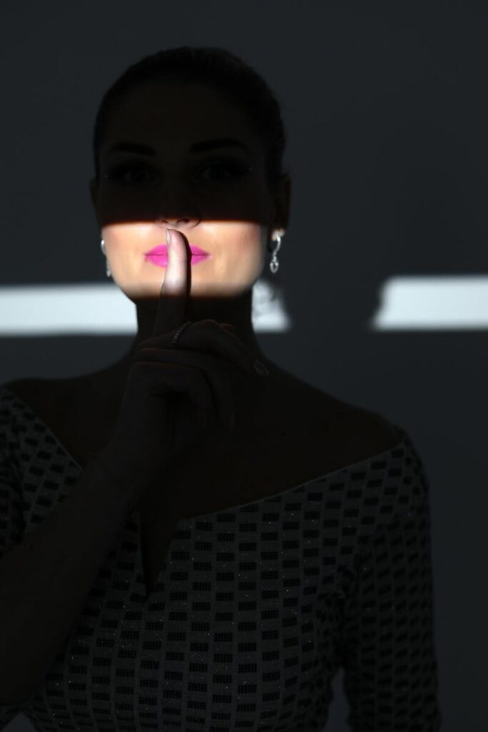 Silhouette of a woman in shadow with finger on lips indicating silence.