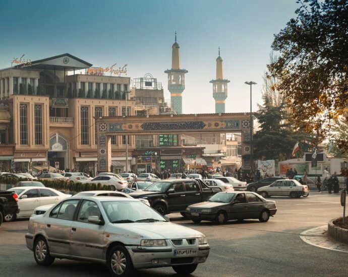 Bustling Tehran street scene with cars, mosque minarets, and traditional architecture.