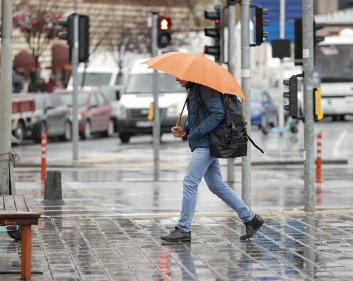 A man walks with an orange umbrella on a rainy day in Istanbul, Türkiye.
