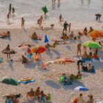 A crowded beach scene with colorful umbrellas and people relaxing in the sunlight.