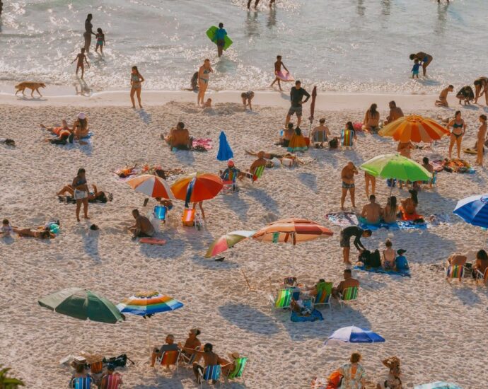 A crowded beach scene with colorful umbrellas and people relaxing in the sunlight.