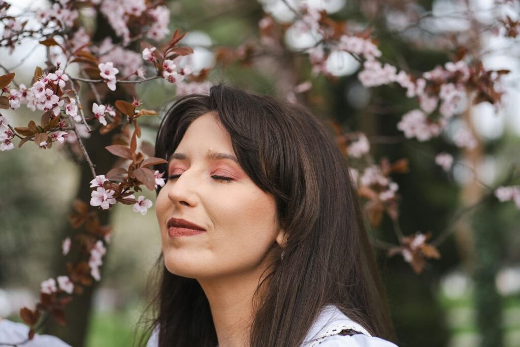 Portrait of a smiling woman enjoying cherry blossoms in a spring garden.