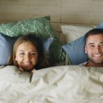 Cheerful couple smiling while relaxing together under cozy linens.