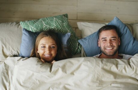 Cheerful couple smiling while relaxing together under cozy linens.