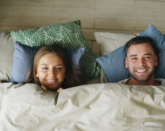 Cheerful couple smiling while relaxing together under cozy linens.