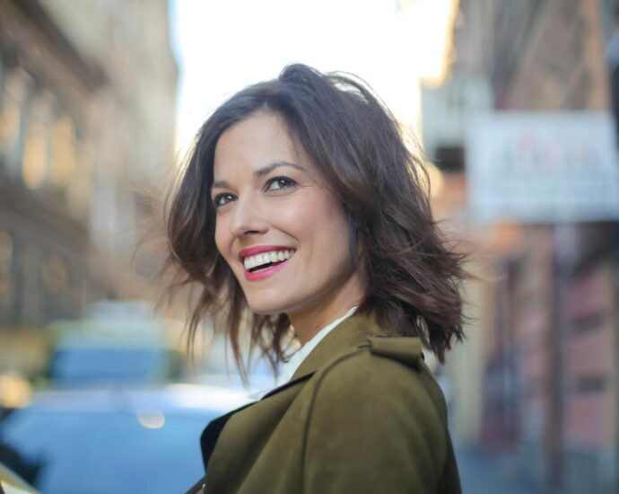 Portrait of a smiling woman standing on a city street in a green coat, looking away delightfully.