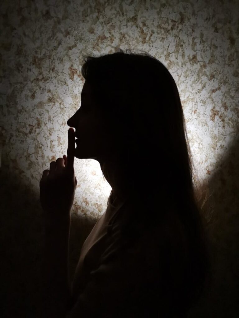 Silhouette of a woman making a quiet gesture against a textured wall background.