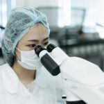A female scientist in protective clothing examines samples using a microscope in a modern laboratory.