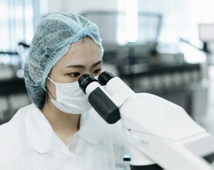 A female scientist in protective clothing examines samples using a microscope in a modern laboratory.