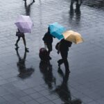 selective color photography of three person holding umbrellas under the rain