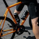 person in black shorts and black nike shoes riding orange and black bicycle