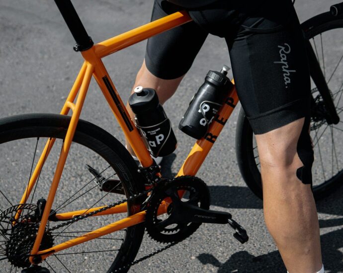 person in black shorts and black nike shoes riding orange and black bicycle