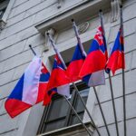 Four slovak flags flying on poles against a building.