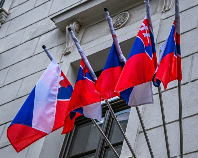 Four slovak flags flying on poles against a building.