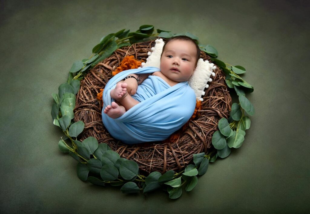Cute baby wrapped in blue blanket, lying in a nest surrounded by leaves.