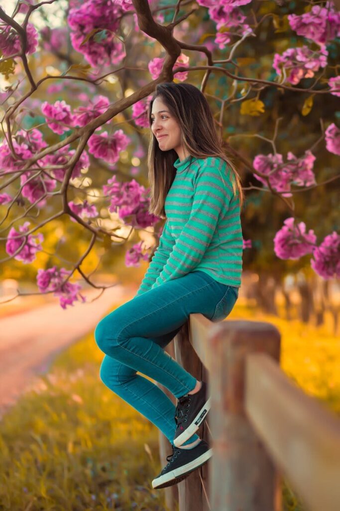 Brunette woman in casual clothing sitting by a tree with pink blossoms on a sunny spring day.