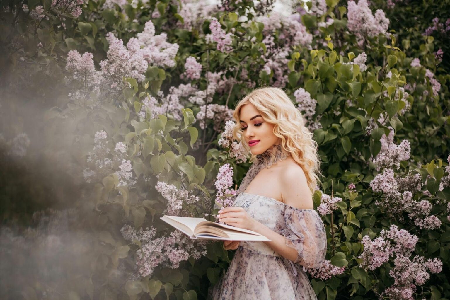 A fashionable woman in a sundress reads a book surrounded by blooming lilacs, exuding springtime elegance.