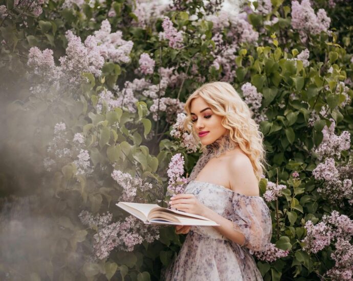A fashionable woman in a sundress reads a book surrounded by blooming lilacs, exuding springtime elegance.
