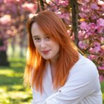 Portrait of a woman with red hair smiling among pink cherry blossoms in spring.