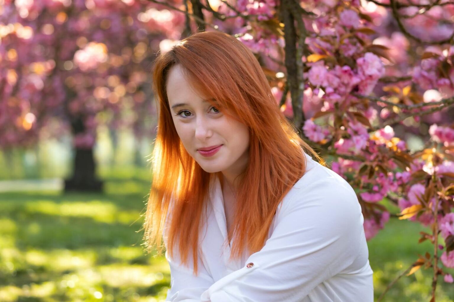 Portrait of a woman with red hair smiling among pink cherry blossoms in spring.