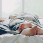 Two people lying in bed under a blanket, relaxing morning scene.