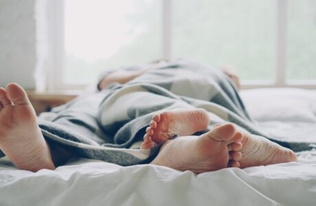 Two people lying in bed under a blanket, relaxing morning scene.